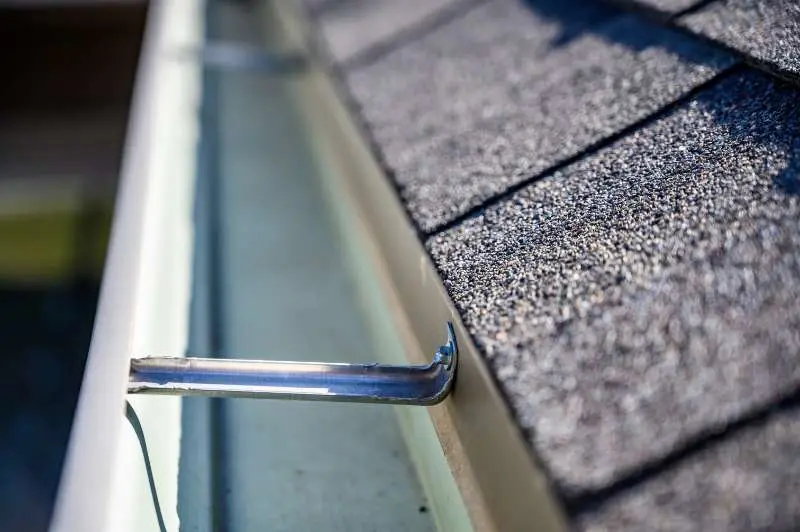 Detailed view of an open aluminum gutter with secure brackets on a roof with asphalt shingles, highlighting professional gutter installation.